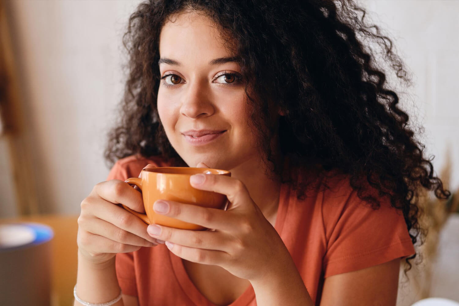 Mulher sorridente de cabelos cacheados segurando uma xícara de café, ilustrando cuidados após clareamento dental em Sergipe.